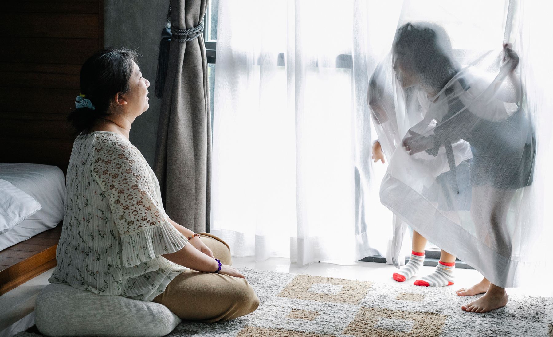 Mother resting at home in morning light while her child plays by the window