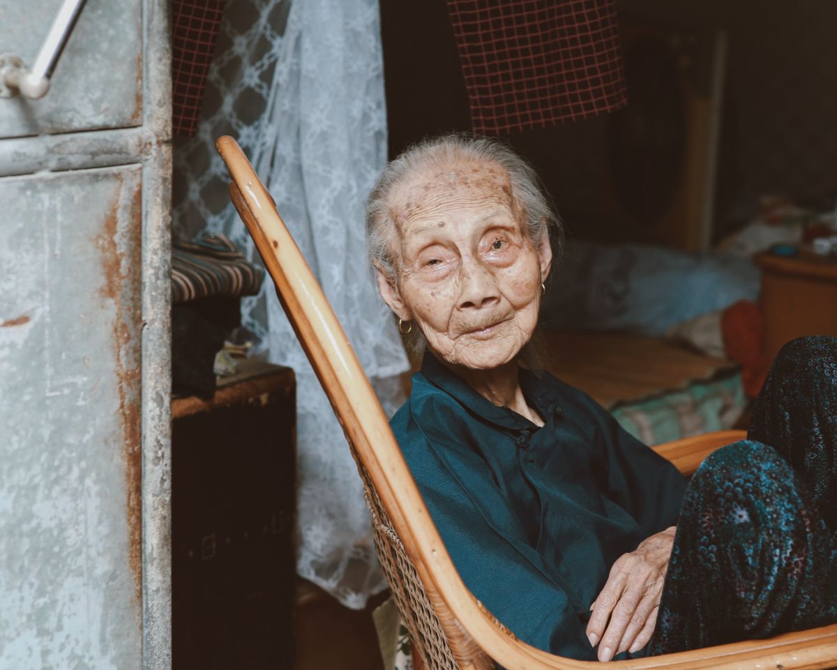 Elderly woman resting in a rattan chair beside a window at home